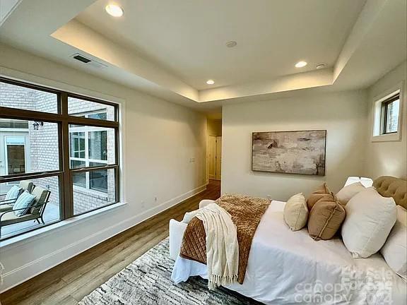 bedroom featuring a tray ceiling, recessed lighting, visible vents, wood finished floors, and baseboards