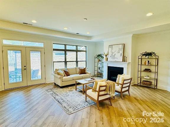 living room featuring light wood finished floors, visible vents, a raised ceiling, french doors, and a fireplace