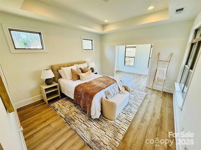 bedroom featuring light wood-style floors, baseboards, visible vents, and a tray ceiling