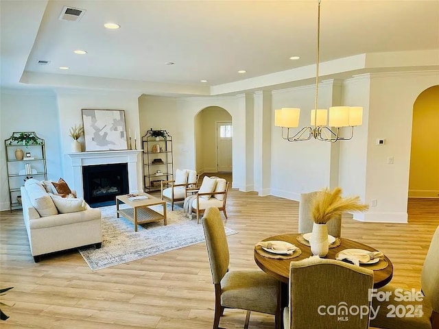 living room featuring arched walkways, a fireplace, a raised ceiling, visible vents, and light wood-type flooring