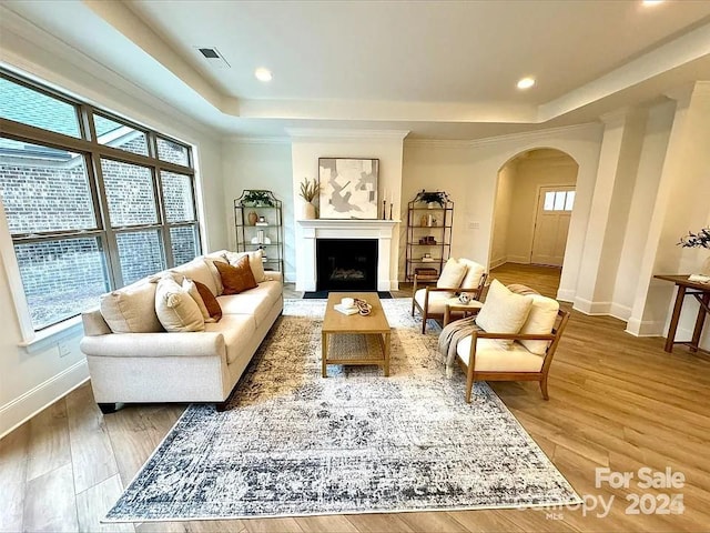 living area with arched walkways, wood finished floors, visible vents, baseboards, and a tray ceiling