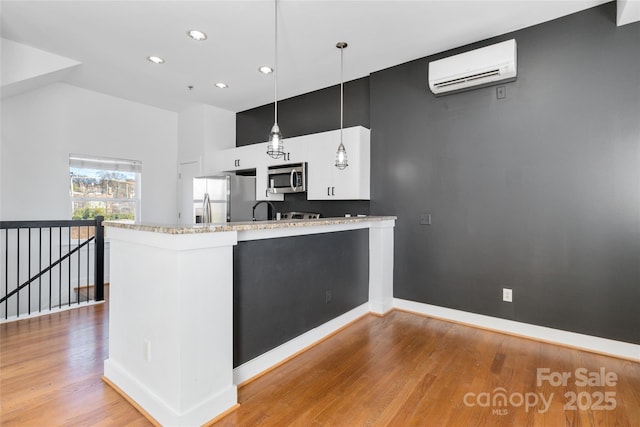 kitchen with kitchen peninsula, stainless steel appliances, a wall mounted AC, white cabinetry, and hanging light fixtures