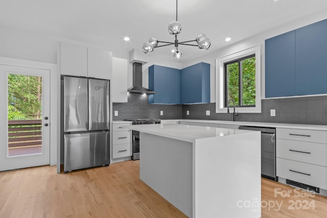 kitchen featuring stainless steel appliances, wall chimney range hood, pendant lighting, light hardwood / wood-style flooring, and a kitchen island