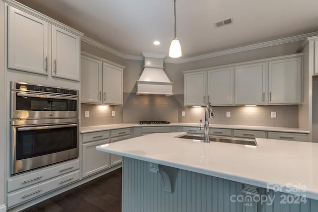 kitchen featuring appliances with stainless steel finishes, premium range hood, crown molding, sink, and pendant lighting