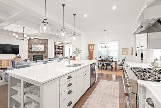 kitchen with coffered ceiling, decorative light fixtures, a center island with sink, a fireplace, and range hood