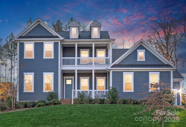view of front facade with a front lawn, a balcony, a standing seam roof, covered porch, and metal roof