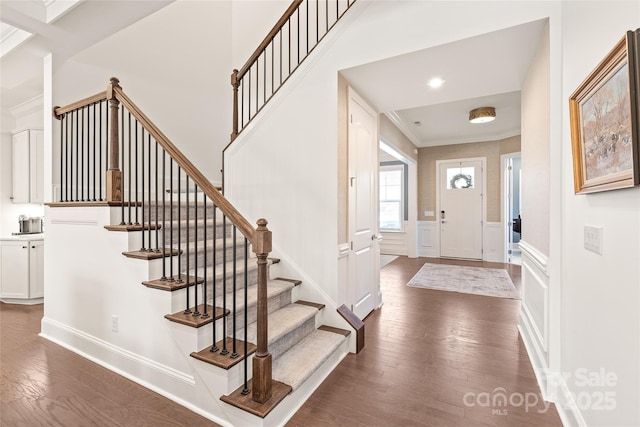 entrance foyer featuring dark wood-style floors, stairs, ornamental molding, and a decorative wall