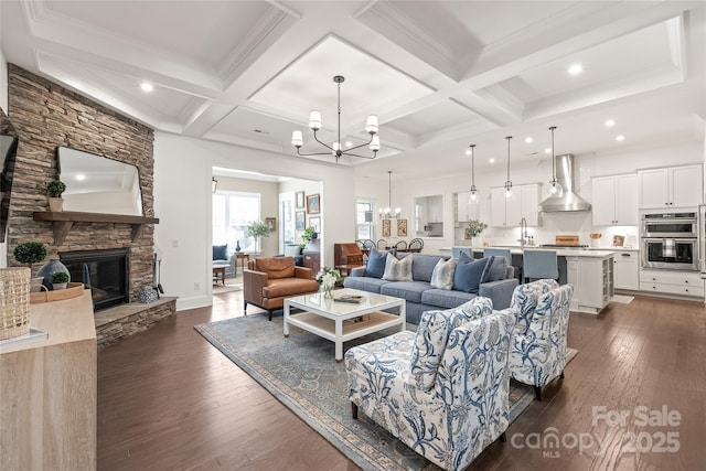 living area with an inviting chandelier, dark wood-style flooring, a stone fireplace, and beam ceiling