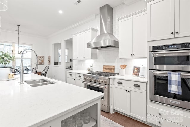 kitchen featuring a sink, decorative backsplash, appliances with stainless steel finishes, wall chimney range hood, and ornamental molding