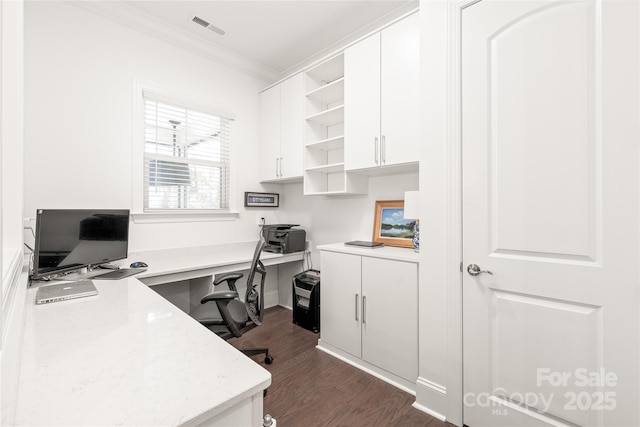 office area with built in study area, visible vents, dark wood-style floors, and crown molding