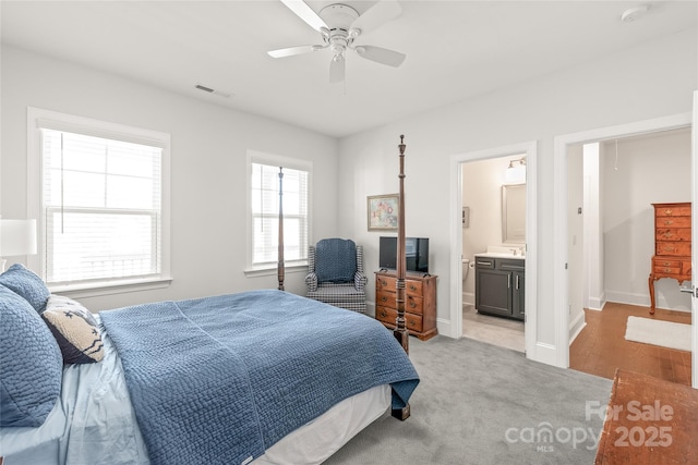 bedroom with a ceiling fan, baseboards, light colored carpet, ensuite bath, and visible vents