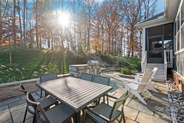 view of patio featuring an outdoor kitchen, area for grilling, entry steps, outdoor dining space, and a sunroom