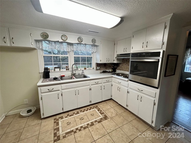 kitchen with ornamental molding, stainless steel oven, sink, light tile patterned floors, and white cabinetry