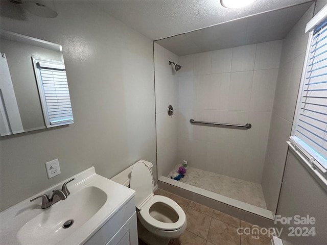 bathroom with tiled shower, tile patterned floors, vanity, and toilet