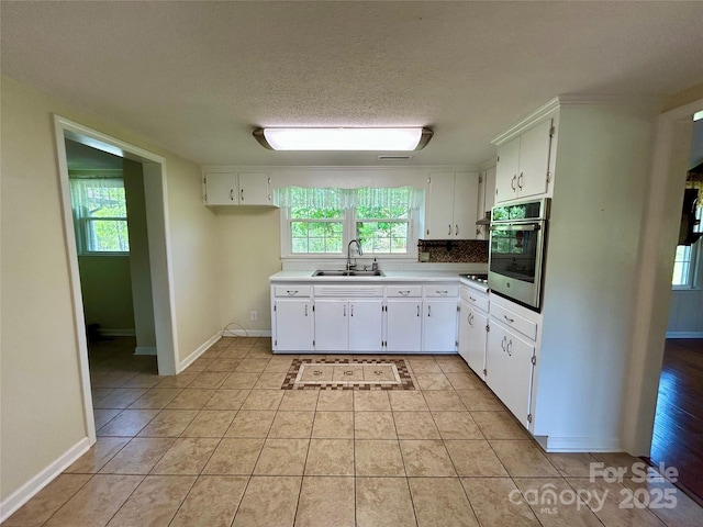 kitchen with oven, white cabinetry, and a sink
