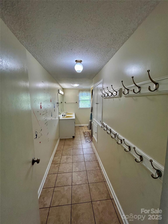 corridor with baseboards, a sink, a textured ceiling, and light tile patterned flooring