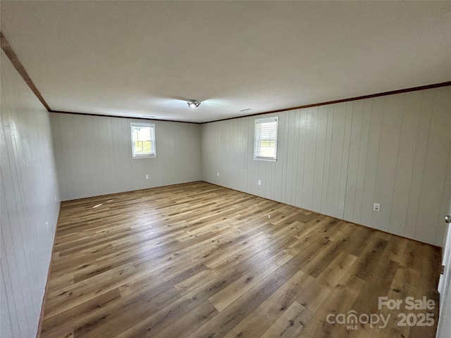 empty room featuring wooden walls, wood finished floors, and ornamental molding