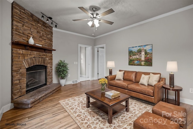 living room featuring crown molding, a textured ceiling, light wood-type flooring, ceiling fan, and a fireplace