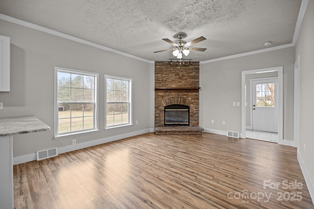 unfurnished living room with crown molding, ceiling fan, a fireplace, a textured ceiling, and light wood-type flooring