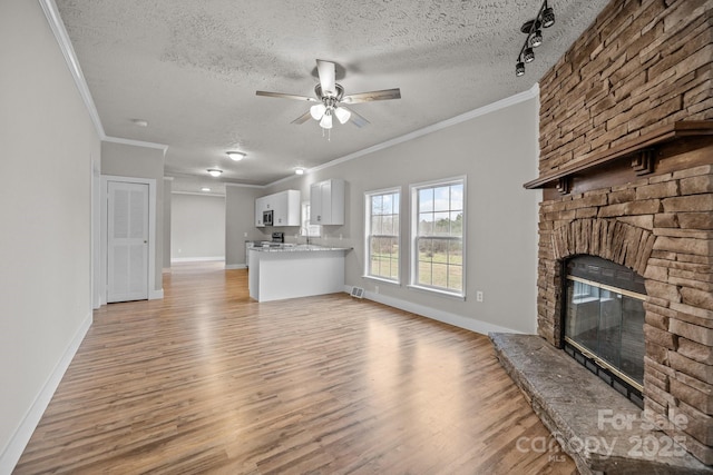 unfurnished living room featuring ornamental molding, a textured ceiling, a fireplace, and light hardwood / wood-style flooring