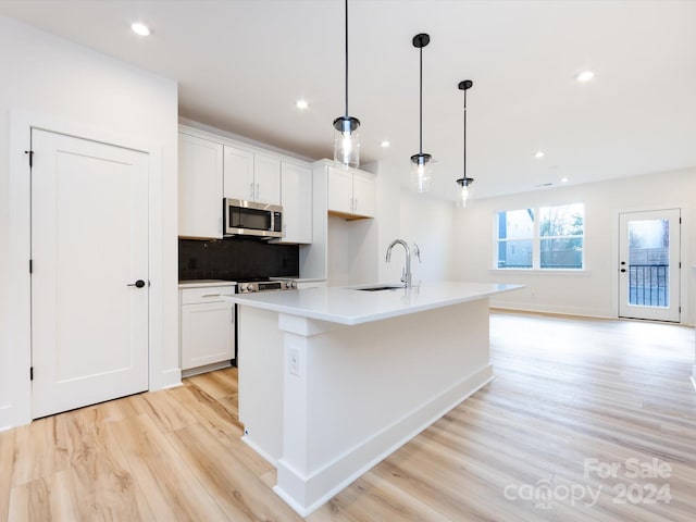 kitchen featuring pendant lighting, a kitchen island with sink, sink, light wood-type flooring, and white cabinetry