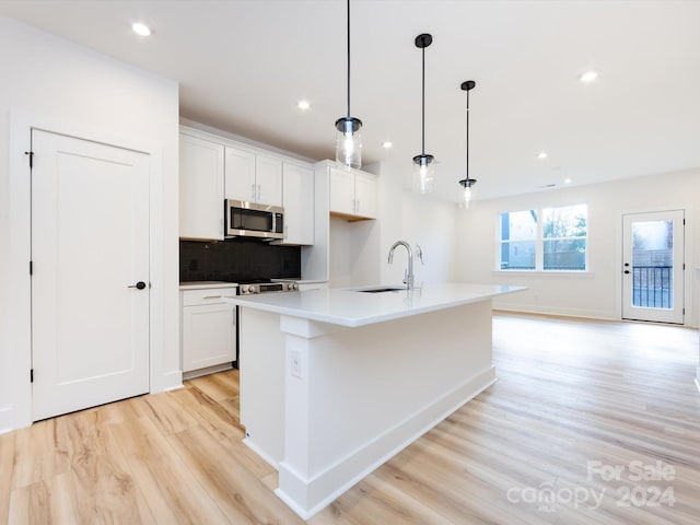 7022 Impulse Ct, Charlotte, NC 28205 - kitchen with stainless steel microwave, light wood-type flooring, decorative backsplash, a kitchen island with sink, and white cabinetry