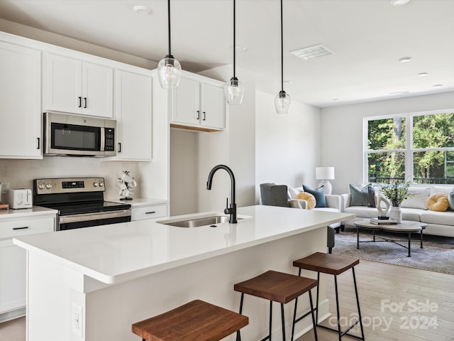 kitchen featuring sink, light hardwood / wood-style flooring, an island with sink, pendant lighting, and appliances with stainless steel finishes