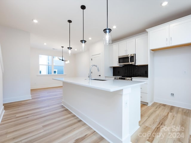 kitchen featuring a kitchen island with sink, sink, pendant lighting, and light wood-type flooring