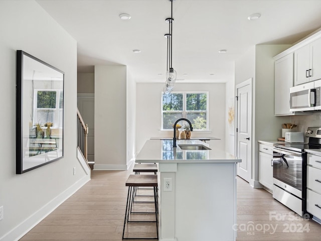 kitchen featuring pendant lighting, a kitchen island with sink, sink, appliances with stainless steel finishes, and white cabinetry