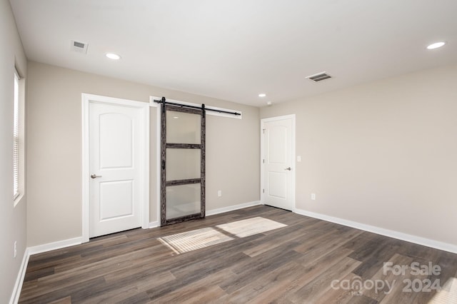 unfurnished bedroom featuring a barn door and dark wood-type flooring