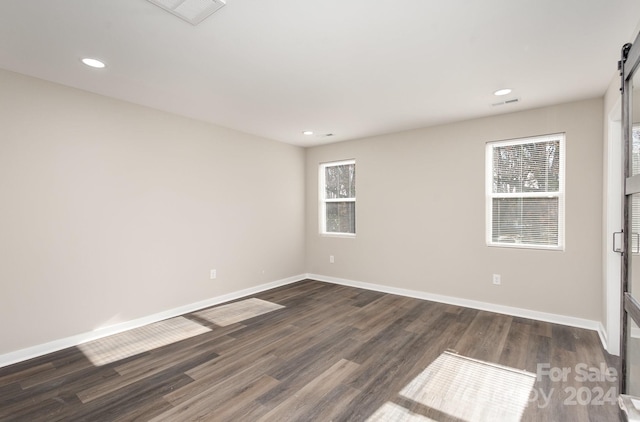 spare room with a barn door and dark wood-type flooring