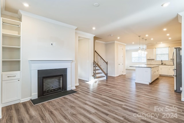 unfurnished living room featuring light hardwood / wood-style floors, ornamental molding, and sink