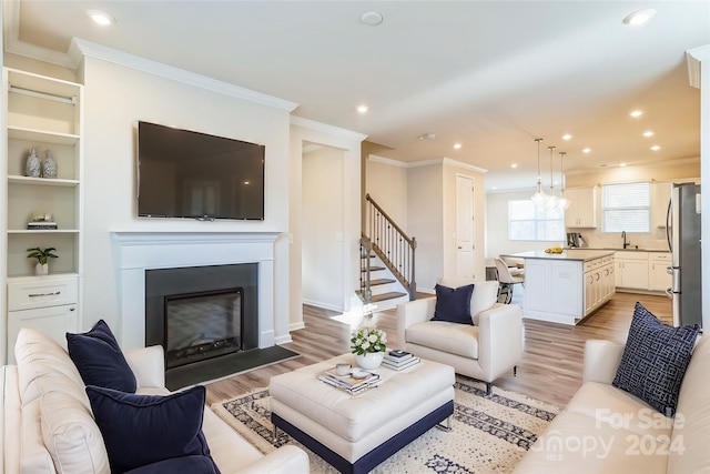 living room featuring sink, ornamental molding, and light hardwood / wood-style flooring