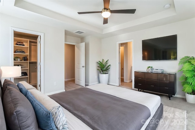 bedroom with light carpet, a walk in closet, a tray ceiling, ceiling fan, and a closet