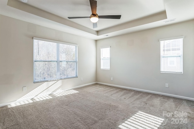 empty room with ceiling fan, a healthy amount of sunlight, and a raised ceiling