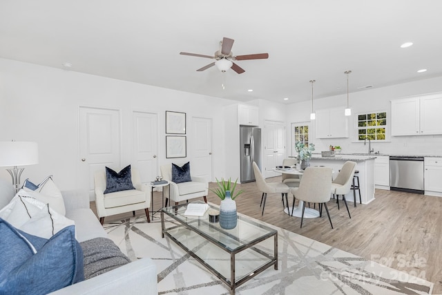 living room with light wood-type flooring, ceiling fan, and sink