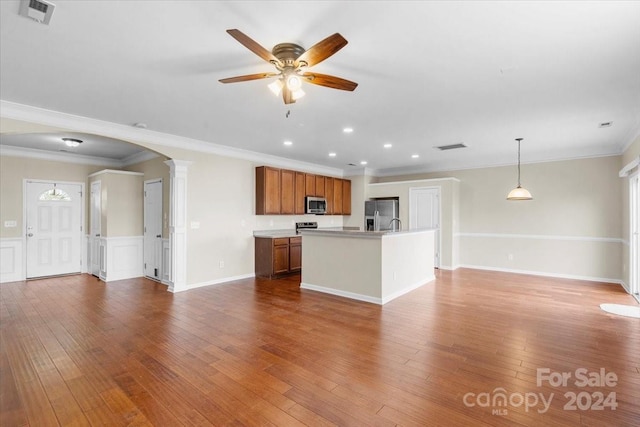 kitchen with hardwood / wood-style floors, an island with sink, decorative light fixtures, appliances with stainless steel finishes, and ornamental molding