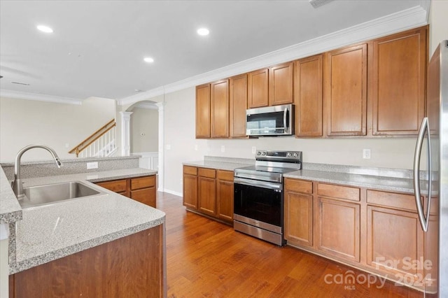 kitchen with sink, dark wood-type flooring, a center island with sink, appliances with stainless steel finishes, and ornamental molding