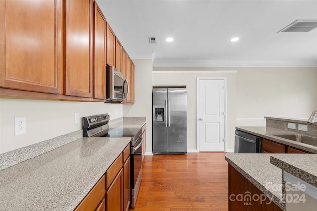 kitchen with appliances with stainless steel finishes, light hardwood / wood-style floors, crown molding, and sink