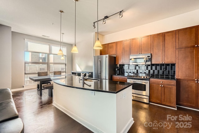 kitchen with tasteful backsplash, dark hardwood / wood-style flooring, an island with sink, pendant lighting, and appliances with stainless steel finishes