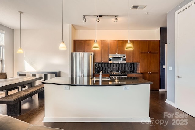 kitchen with a center island with sink, decorative light fixtures, backsplash, and appliances with stainless steel finishes