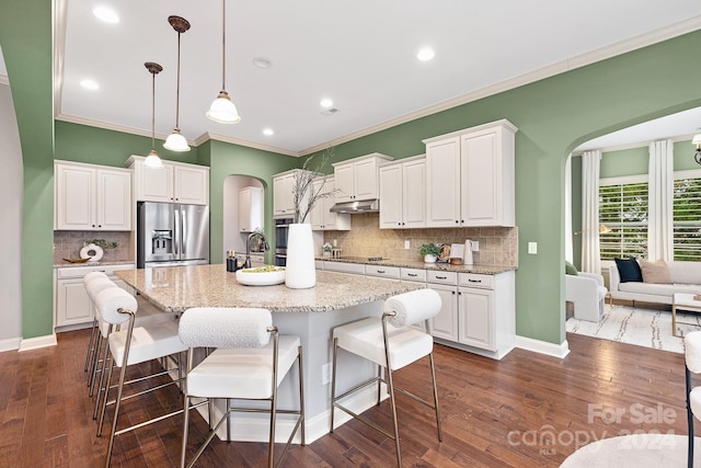 kitchen featuring white cabinets, decorative light fixtures, a center island with sink, and appliances with stainless steel finishes