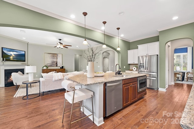 kitchen featuring white cabinetry, sink, stainless steel appliances, light stone counters, and a kitchen island with sink