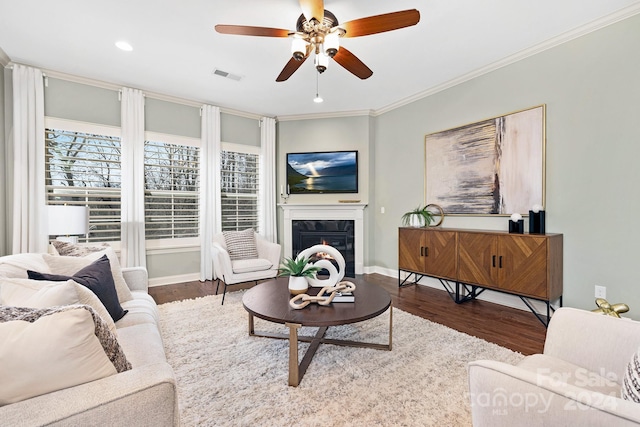 living room with a tile fireplace, ceiling fan, wood-type flooring, and ornamental molding