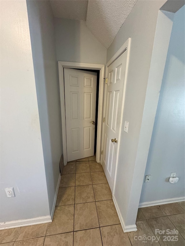 hallway with a textured ceiling, light tile patterned floors, and vaulted ceiling