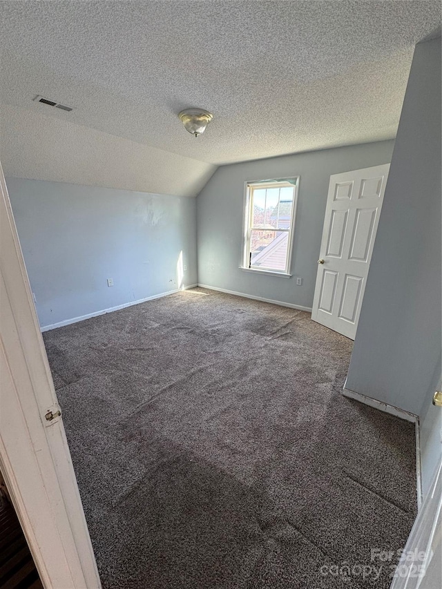 interior space featuring dark carpet, a textured ceiling, and lofted ceiling