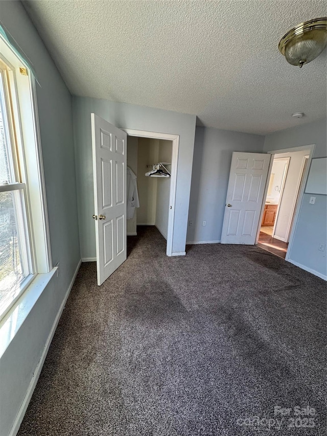 unfurnished bedroom with a closet, dark carpet, a walk in closet, and a textured ceiling