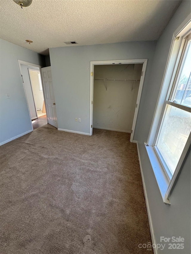 unfurnished bedroom with light carpet, multiple windows, a textured ceiling, and a closet