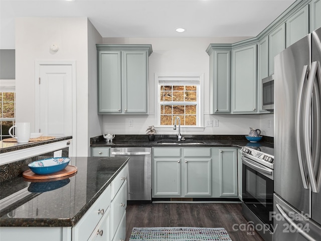 kitchen with appliances with stainless steel finishes, dark wood-type flooring, dark stone countertops, and sink