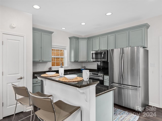 kitchen with dark wood-type flooring, stainless steel appliances, a kitchen breakfast bar, dark stone countertops, and a kitchen island